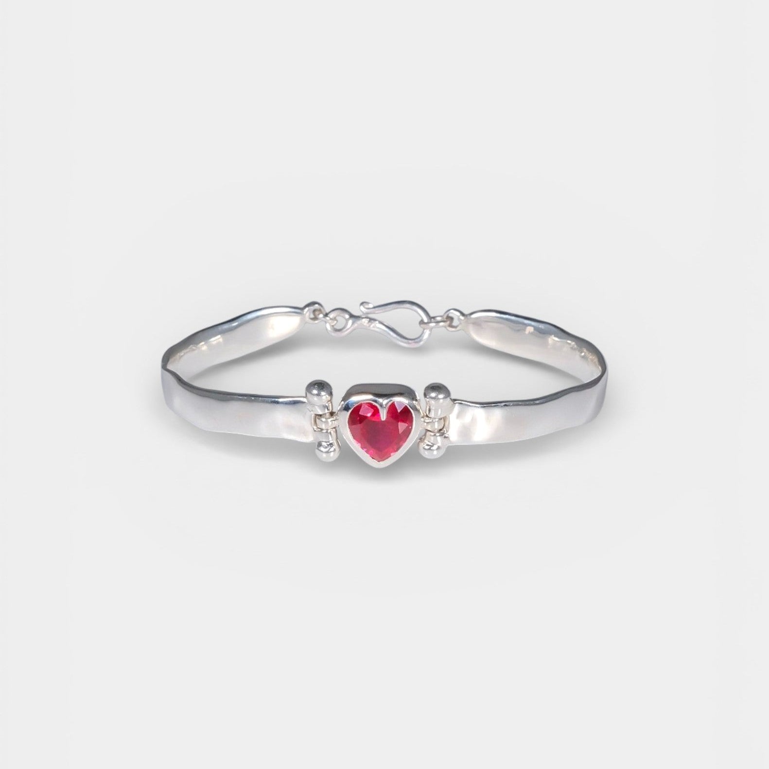 Silver bracelet with a red heart charm on a white background
