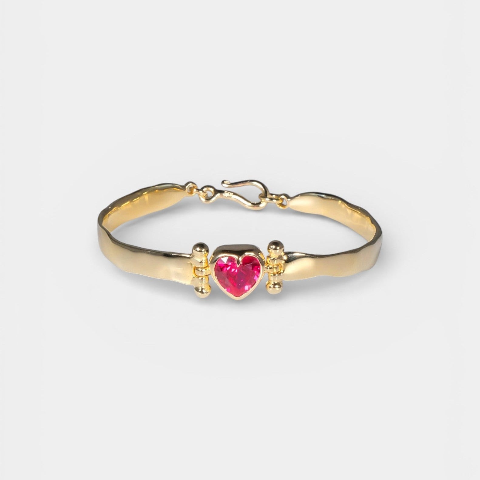 Gold bracelet with a heart-shaped pink gem on a white background