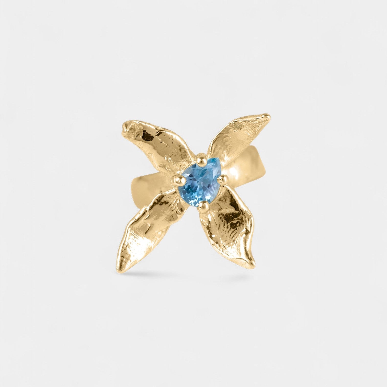 Gold x-shaped ring with a blue gemstone on a white background