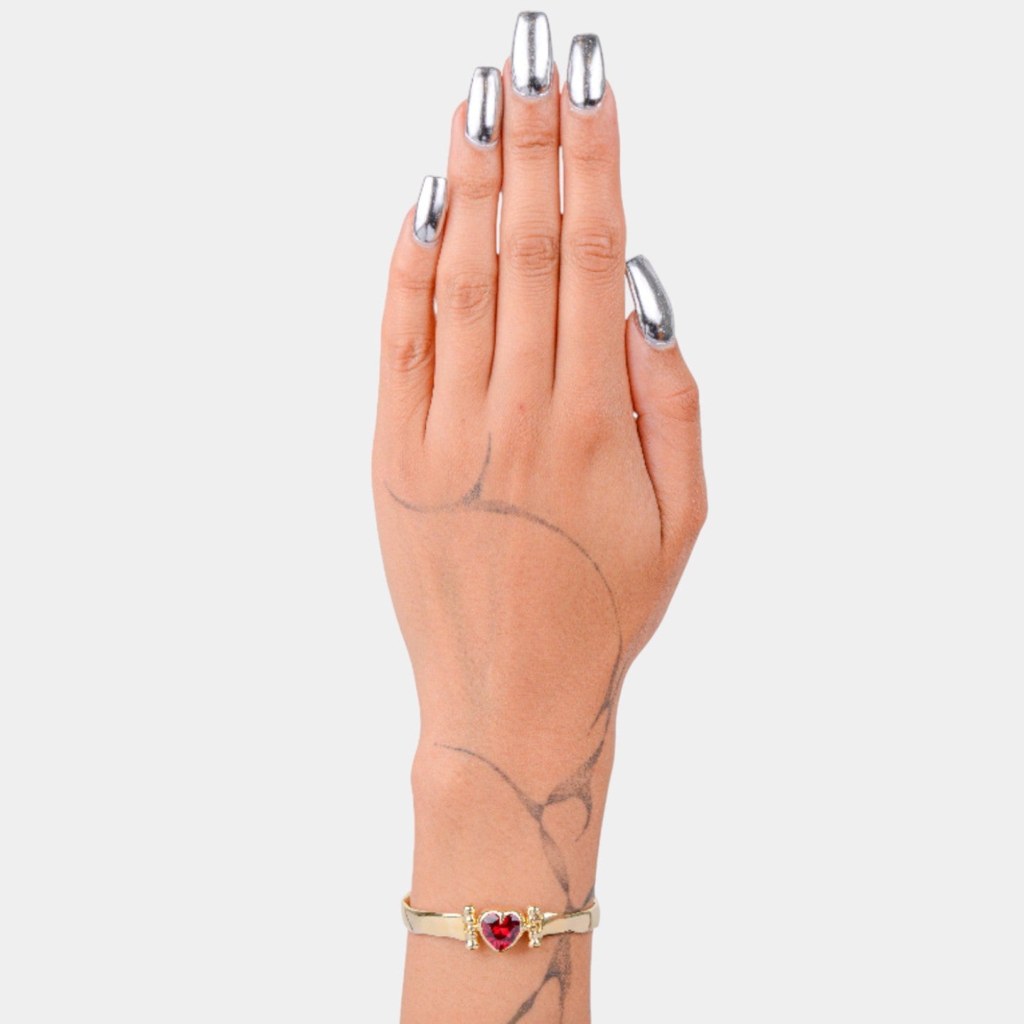 Hand wearing a gold bracelet with a red heart charm on a light gray background