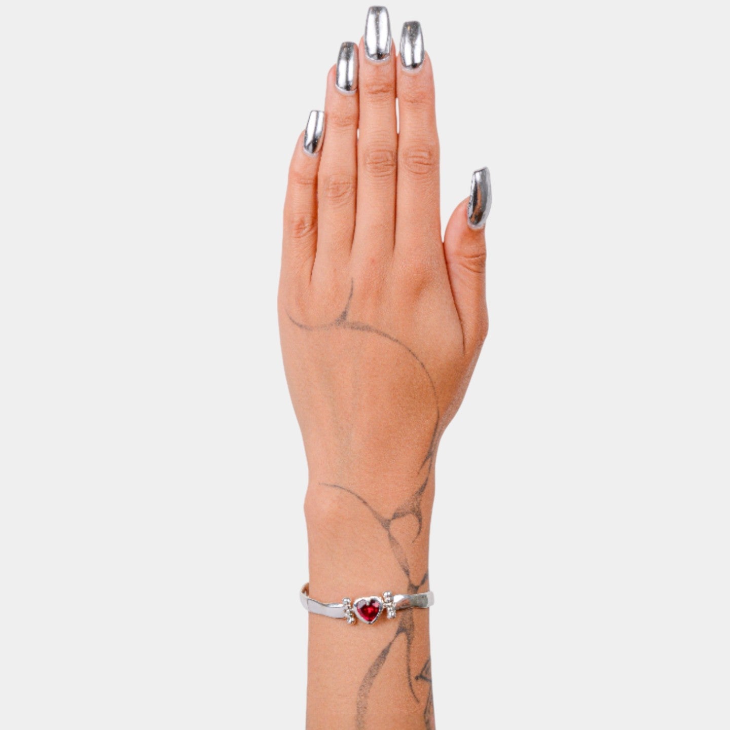 Hand wearing a silver bracelet with a red heart charm on a light gray background