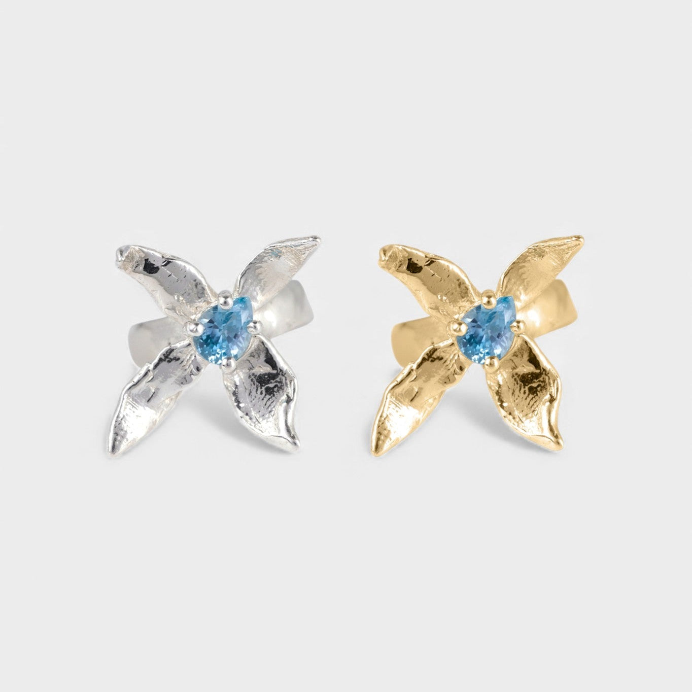 Pair of x-shaped rings in silver and gold with blue gemstone on a white background