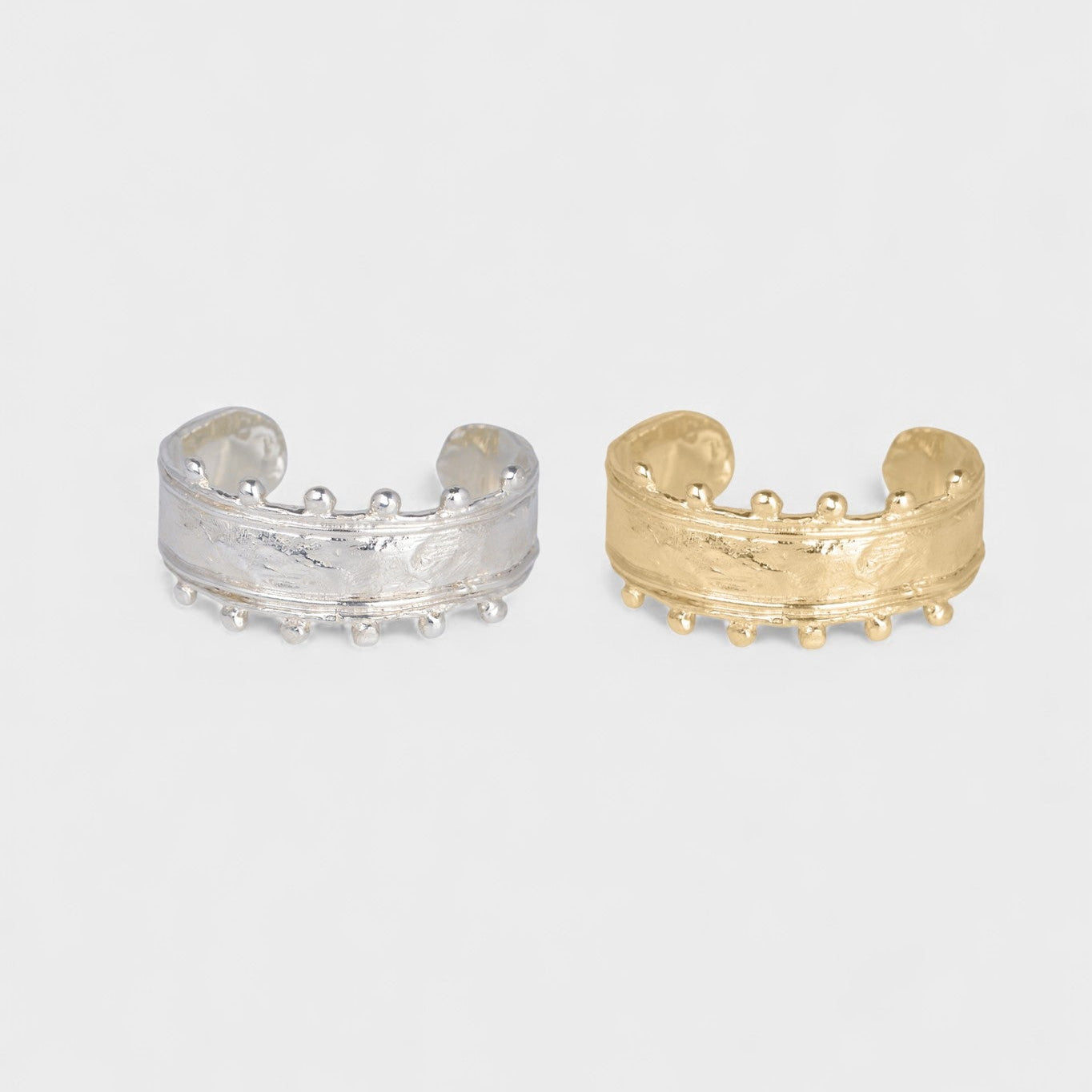 Two gold and silver cuff bracelets on a light gray background