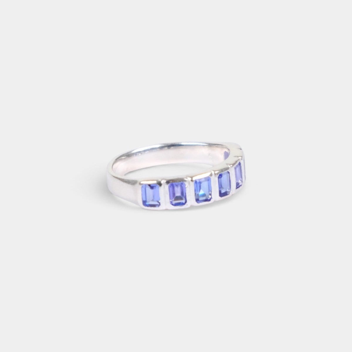 A silver band ring featuring rectangular blue gemstones set in a row, photographed on a light gray background.