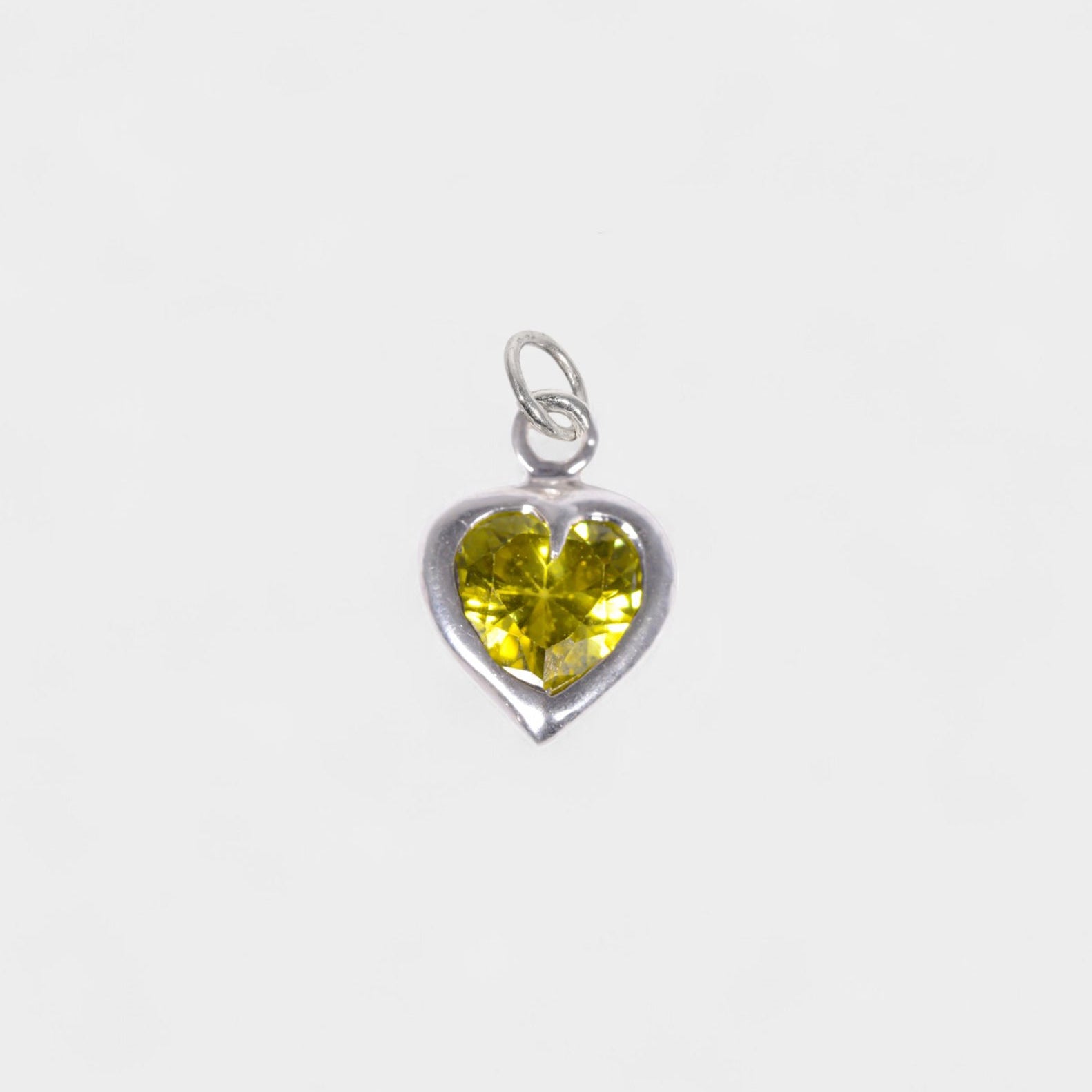 A silver heart-shaped pendant charm featuring a faceted yellow gemstone, shown against a plain light gray background.