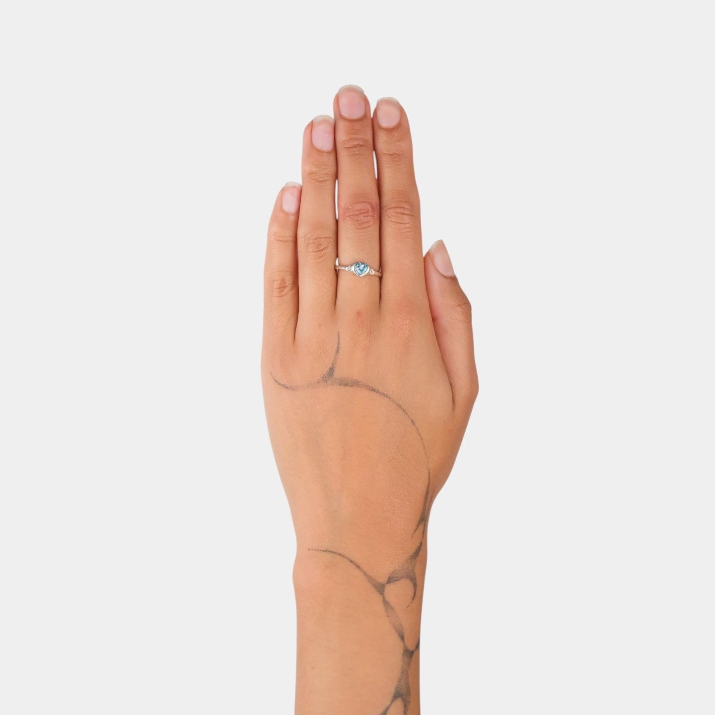 Hand wearing a ring with a blue gemstone on a plain background