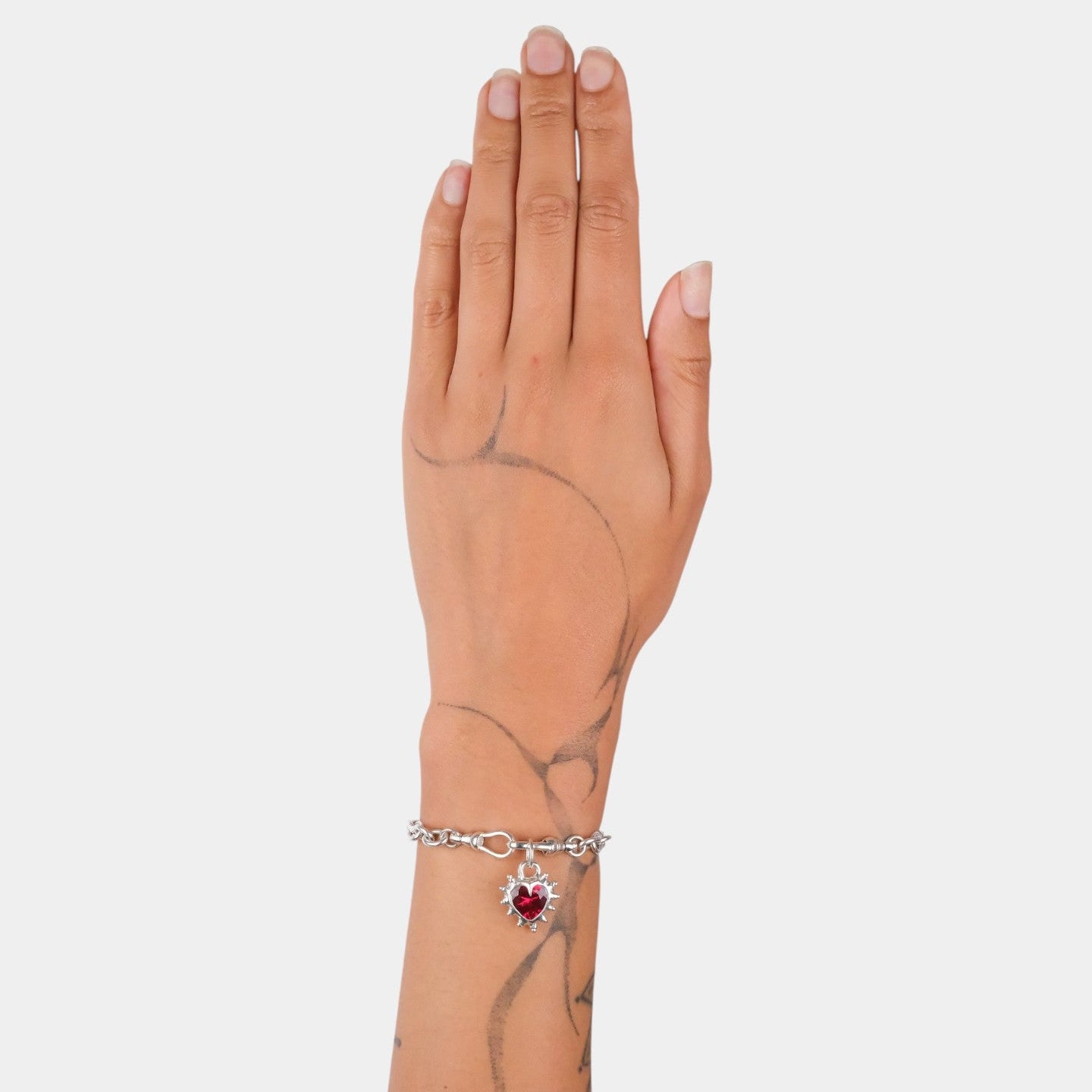 Hand wearing a bracelet with a heart-shaped charm on a plain background