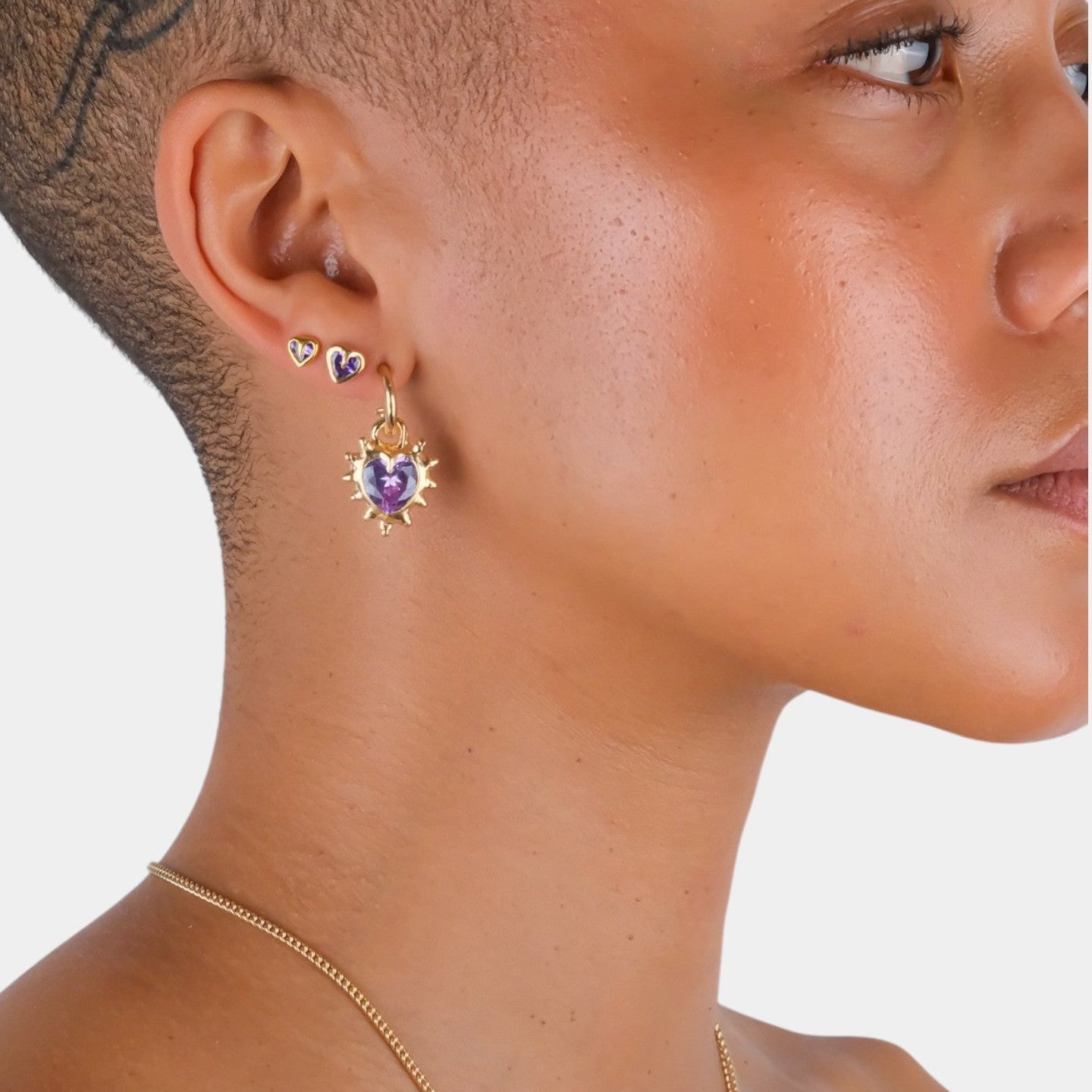 Close-up of a person wearing gold earrings with purple gemstones on a white background