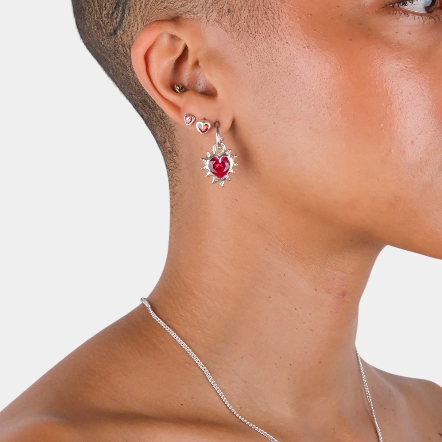 Close-up of a person wearing a silver earring with a red gemstone on a plain background