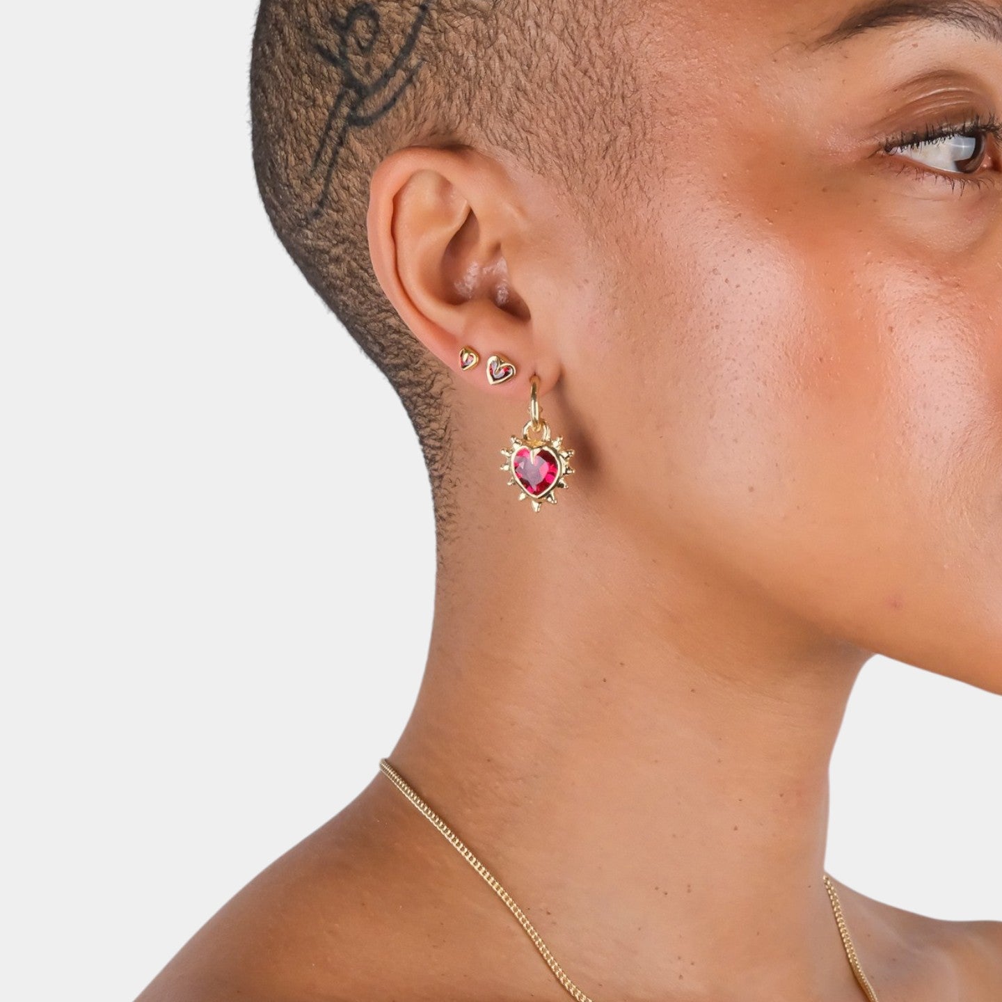 Close-up of a person wearing gold earrings with a red gemstone on a light gray background