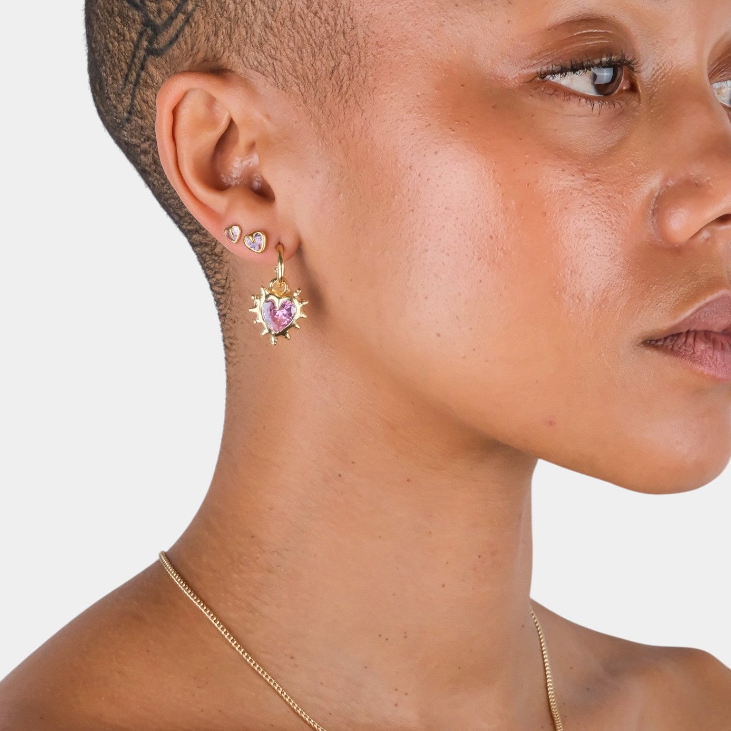 Close-up of a person wearing a gold necklace and pink heart-shaped earrings on a white background