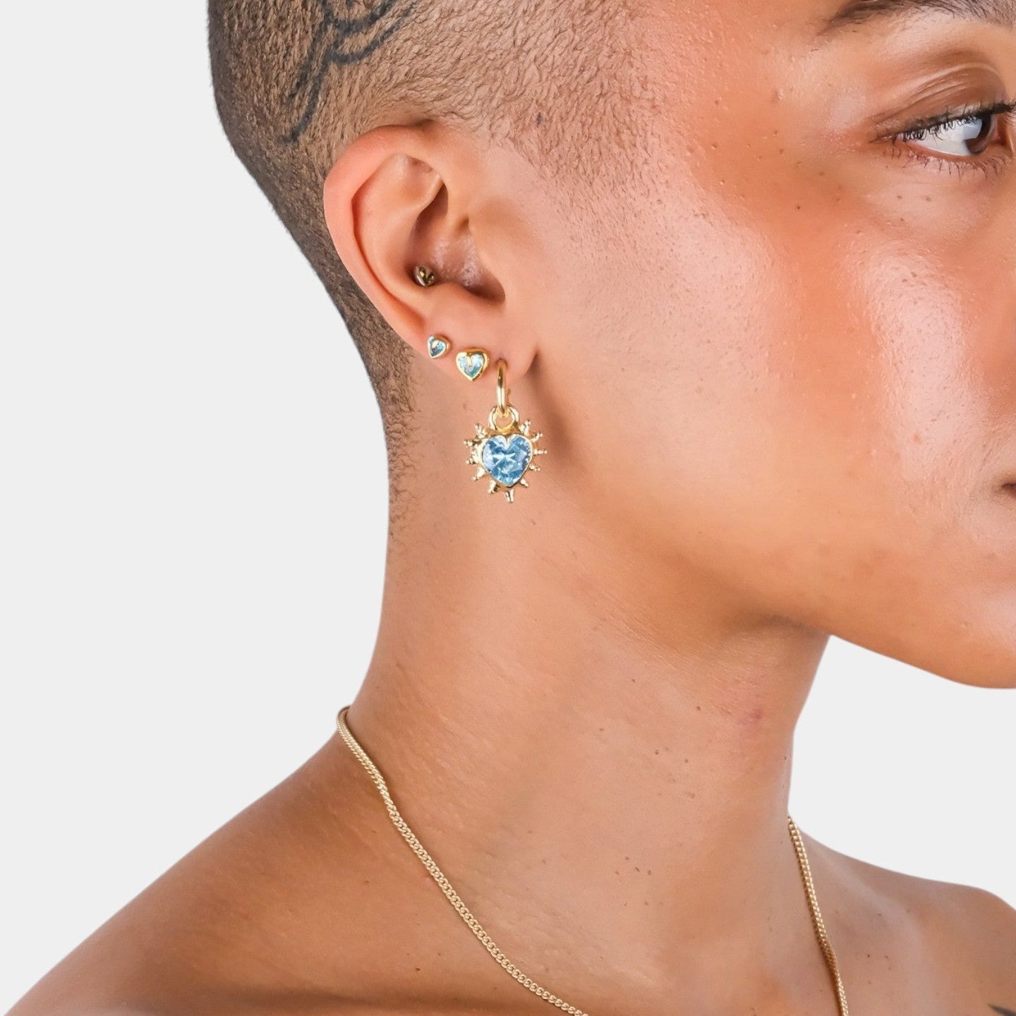 Close-up of a person wearing gold earrings with a blue gemstone on a neutral background
