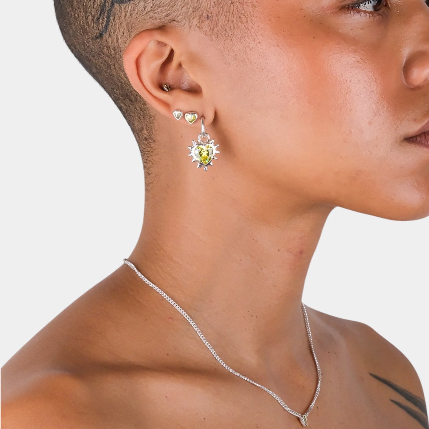 Close-up of a person wearing a silver necklace and earrings on a light gray background