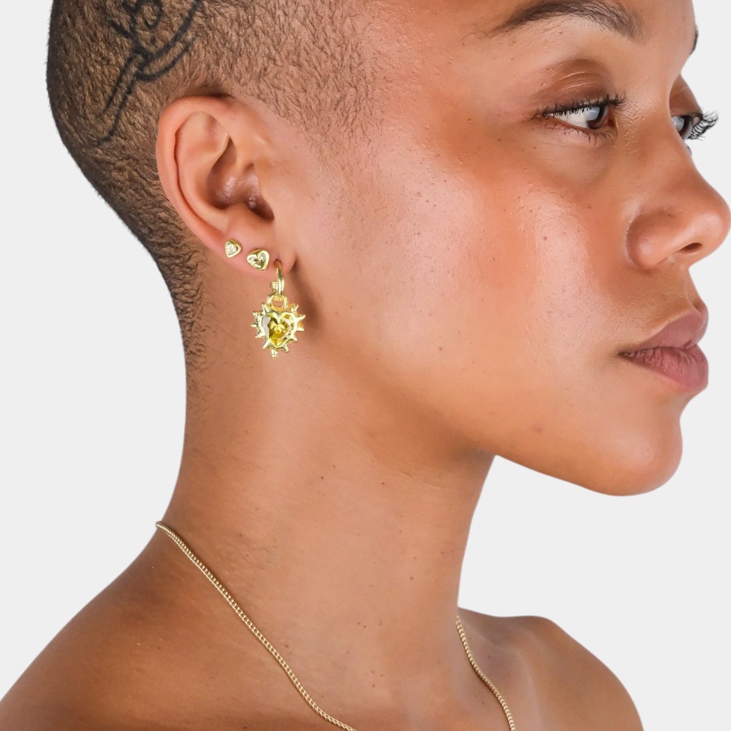 Close-up of a person wearing gold earrings and a necklace on a white background