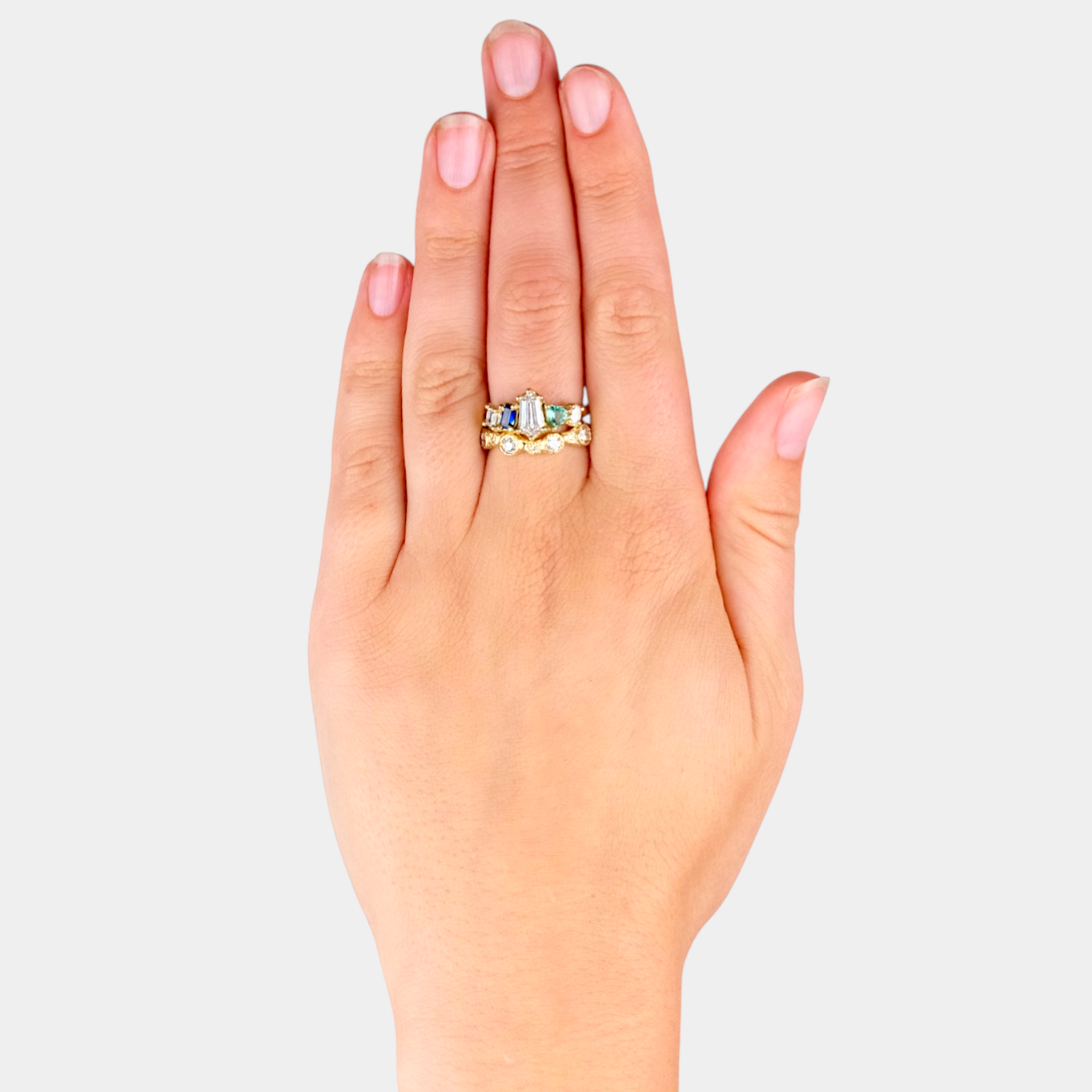 Hand wearing a gold ring with gemstones on a light gray background