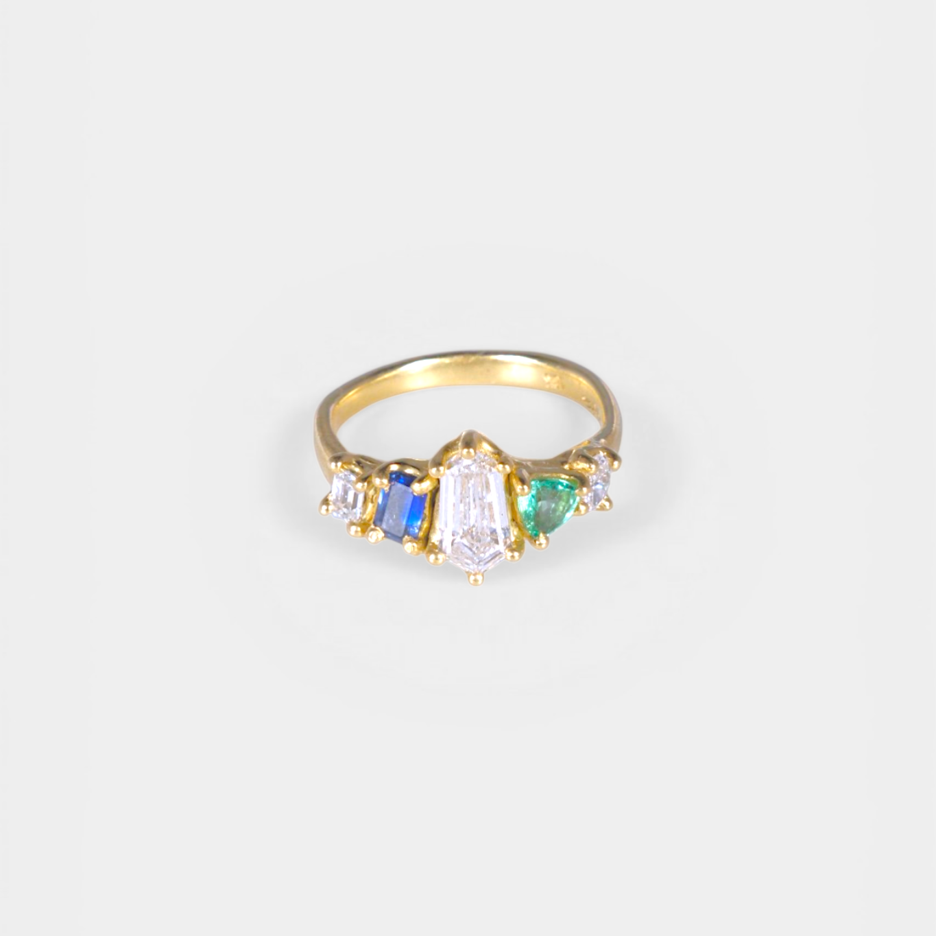 Gold ring with multicolored gemstones on a light gray background