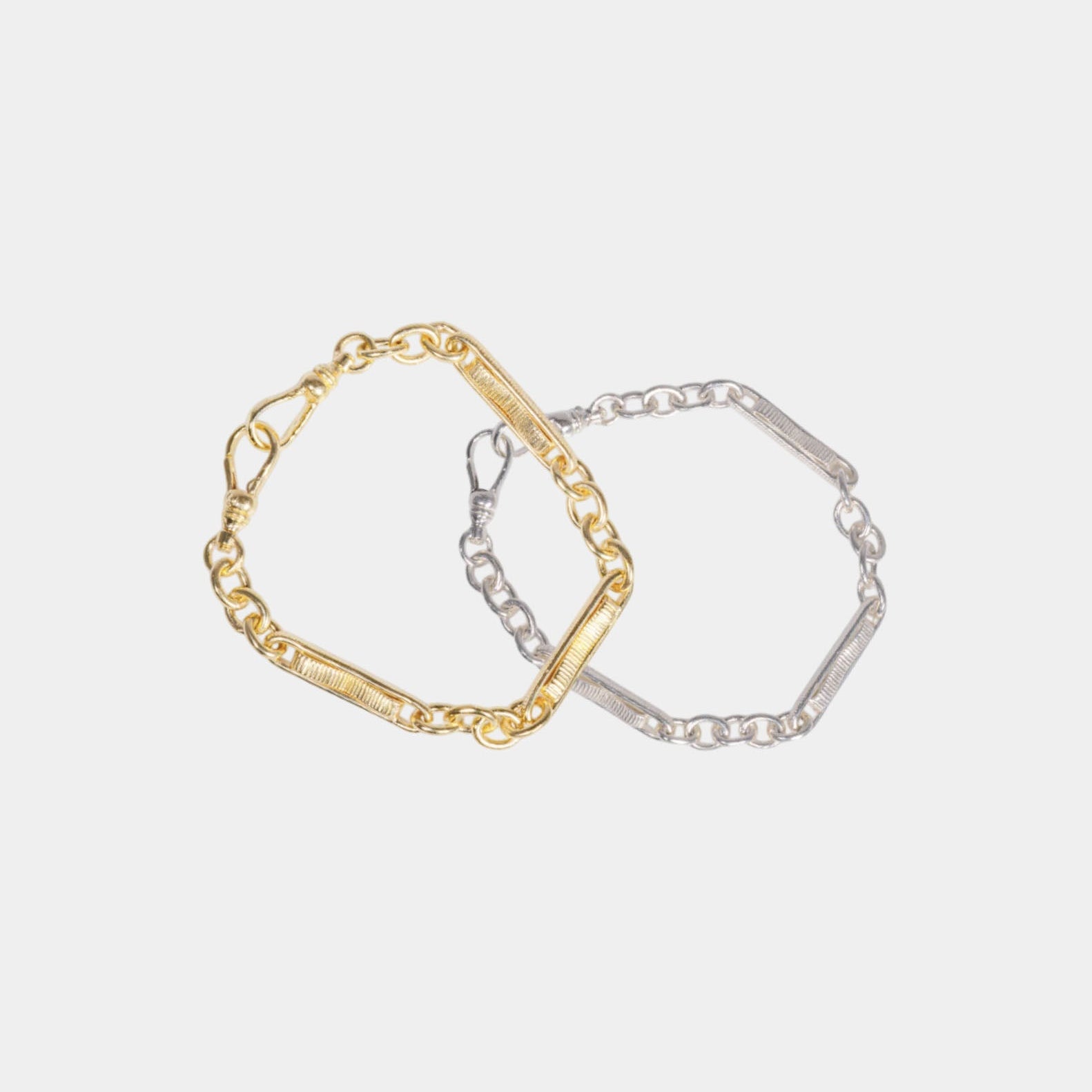 Two bracelets, one in silver and one in gold vermeil, laid on a white surface.