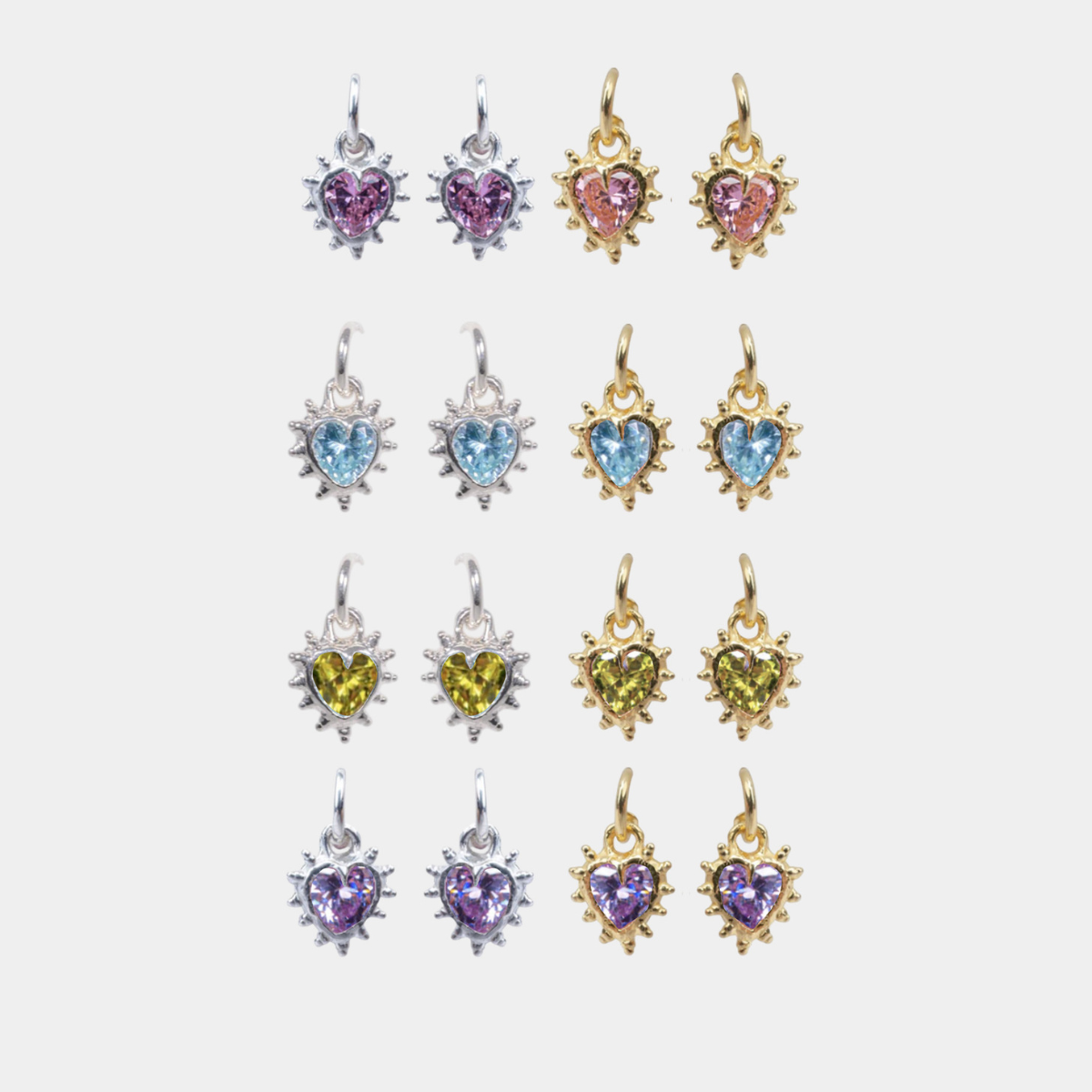 Twelve heart-shaped dangle earrings arranged in a grid on a light gray background. The earrings feature heart-shaped gemstones in purple, pink, blue, and yellow, set in silver and gold-tone metal with starburst details.