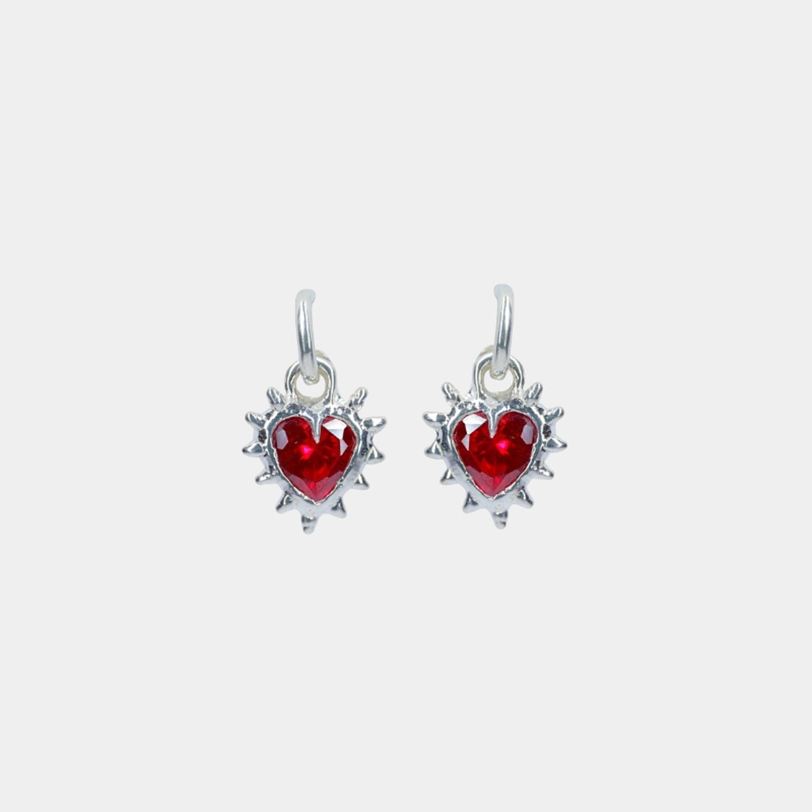 A pair of heart-shaped hoop earrings with ruby red cubic zirconia set in silver metal.