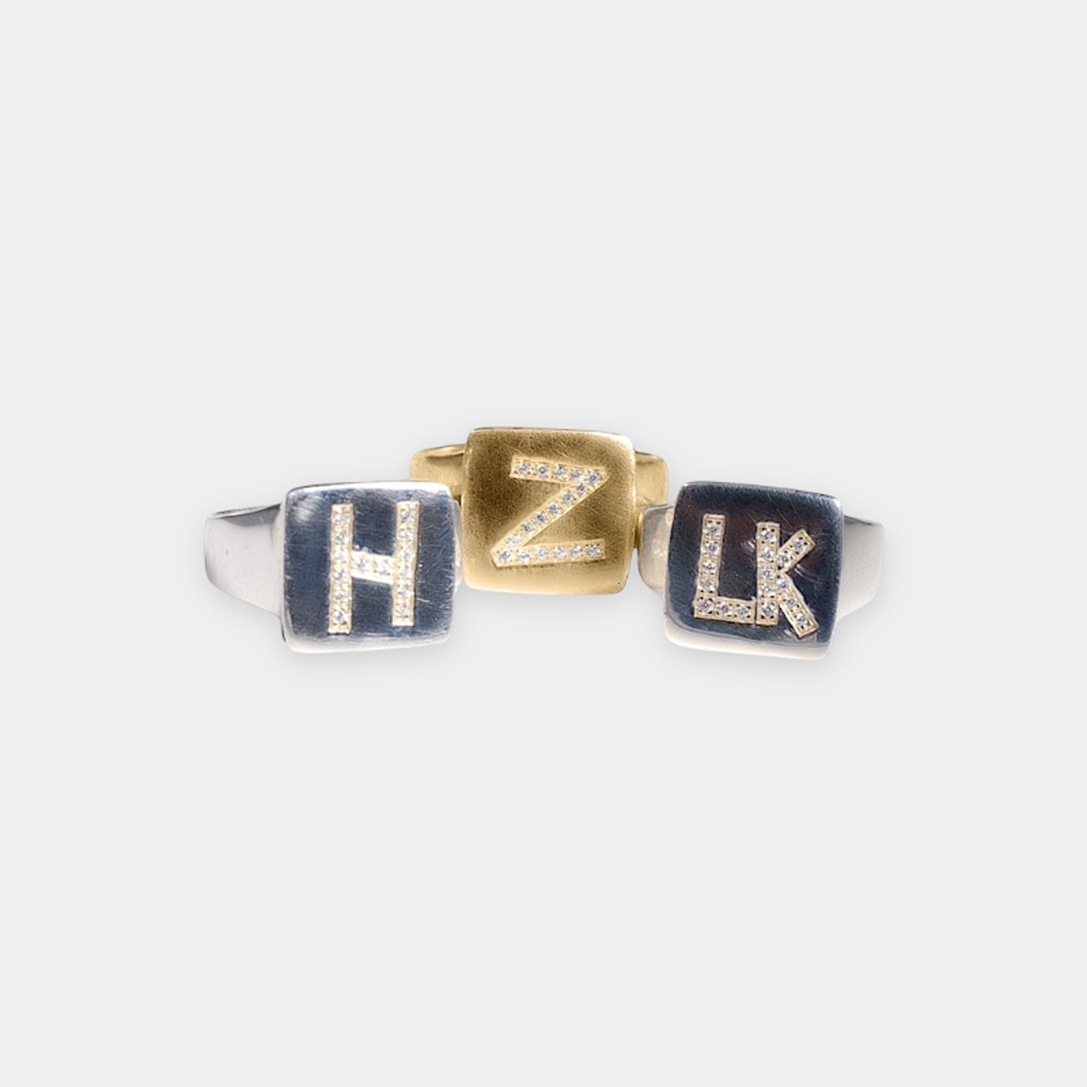 A collection of three signet rings with engraved letters 'H', 'Z', and 'L' on a white background.
