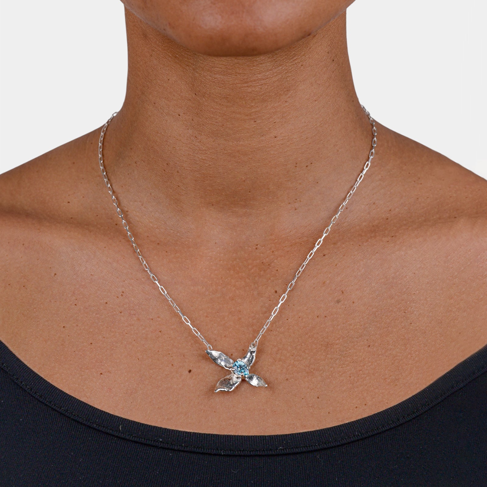 Silver necklace with a blue gemstone pendant on a person wearing a black top.