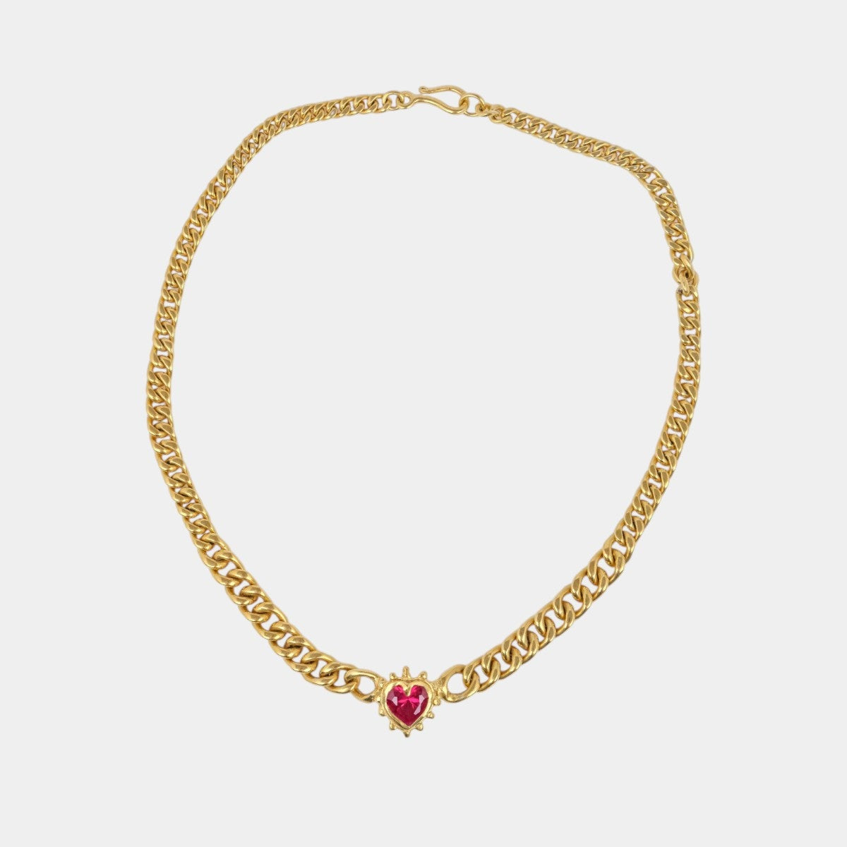 A gold chain necklace featuring a small, heart-shaped pink gemstone pendant, displayed against a solid light gray background.