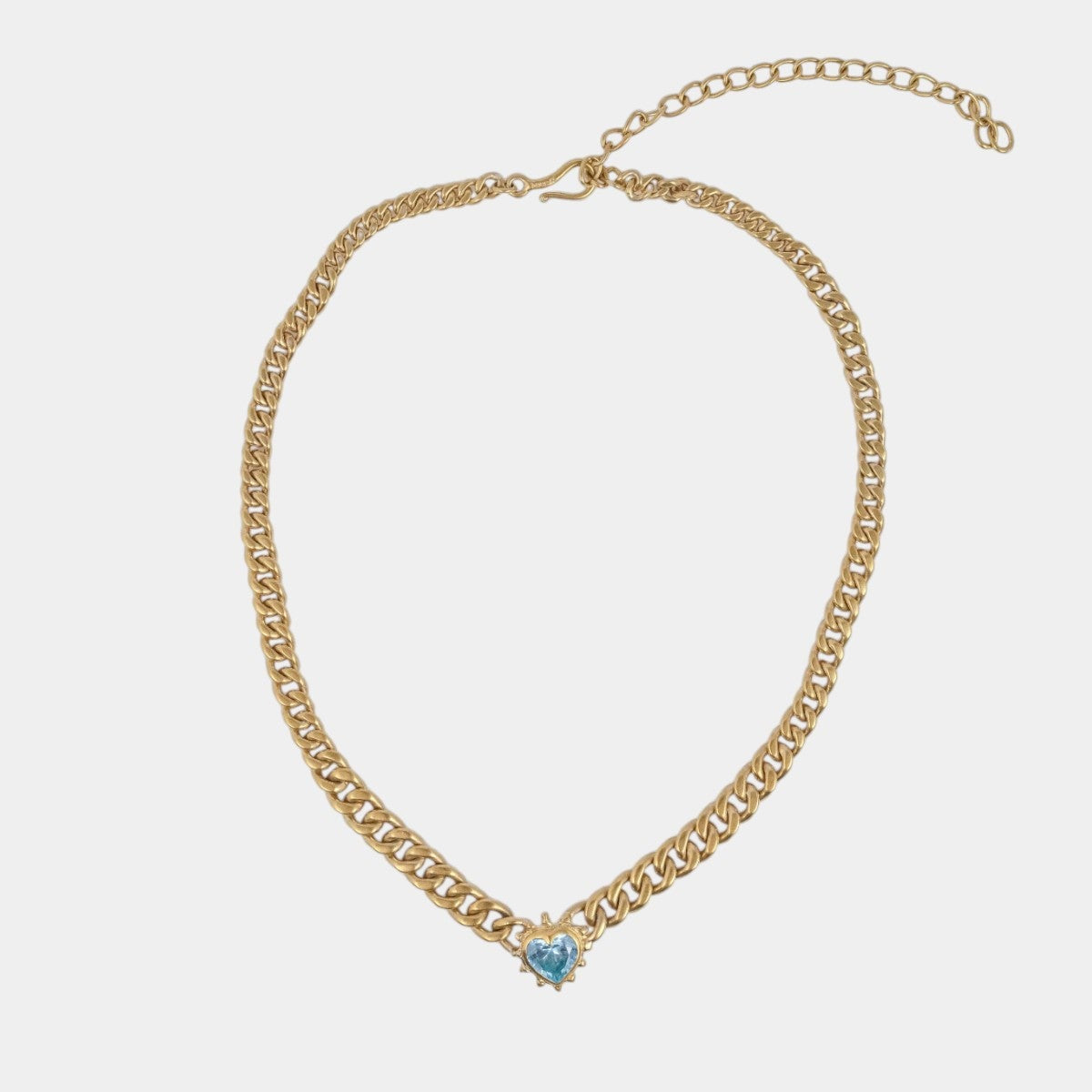 A gold-toned chain necklace with a small light blue heart-shaped charm at the center, displayed on a light gray background.