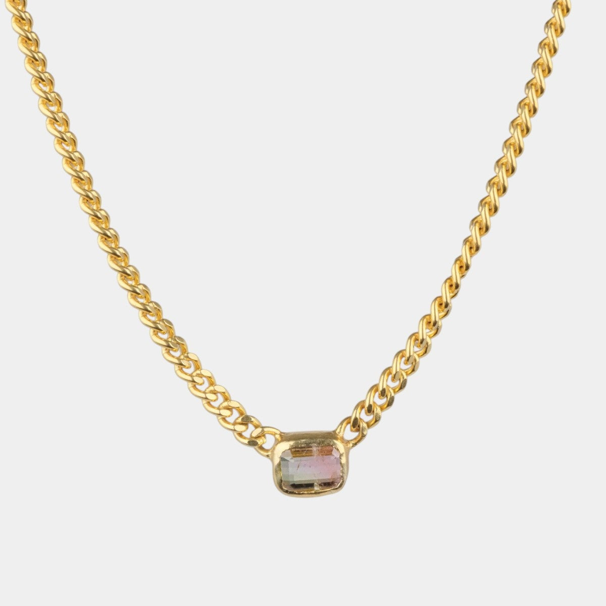 A gold chain necklace with a small rectangular bezel-set iridescent stone pendant, shown against a plain light gray background.