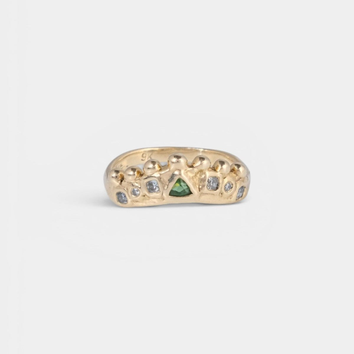 A gold ring with a textured, organic shape, featuring a central green triangular stone and small white stones set along the top, shown on a light gray background.