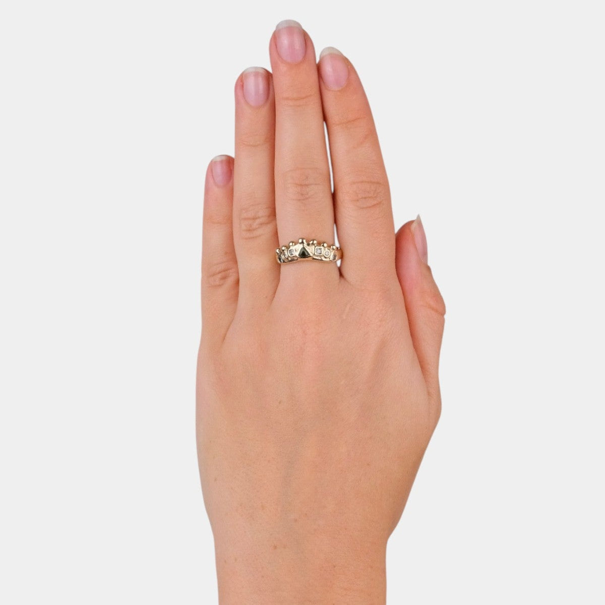 A close-up of a person's hand wearing a delicate gold ring with small clear stones, set against a plain light gray background.