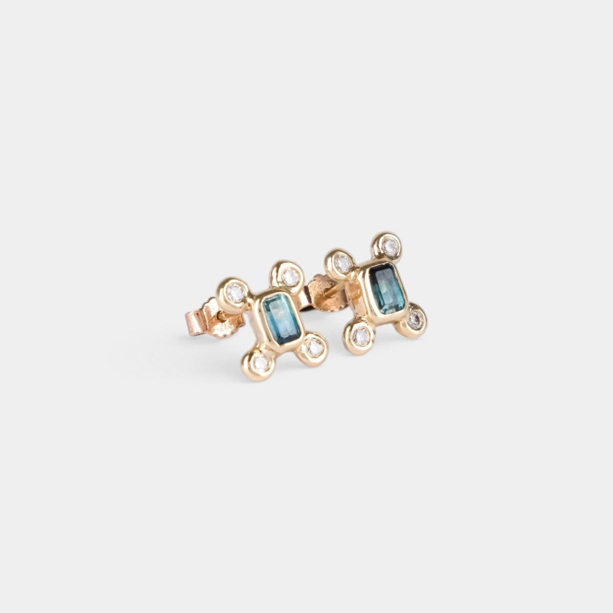 A pair of gold-toned stud earrings featuring rectangular light blue gemstones and small clear accent stones, set against a plain light gray background.