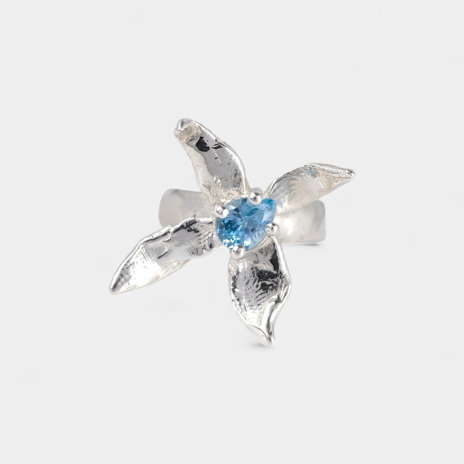 Silver flower shaped ring with blue gemstone on a white background