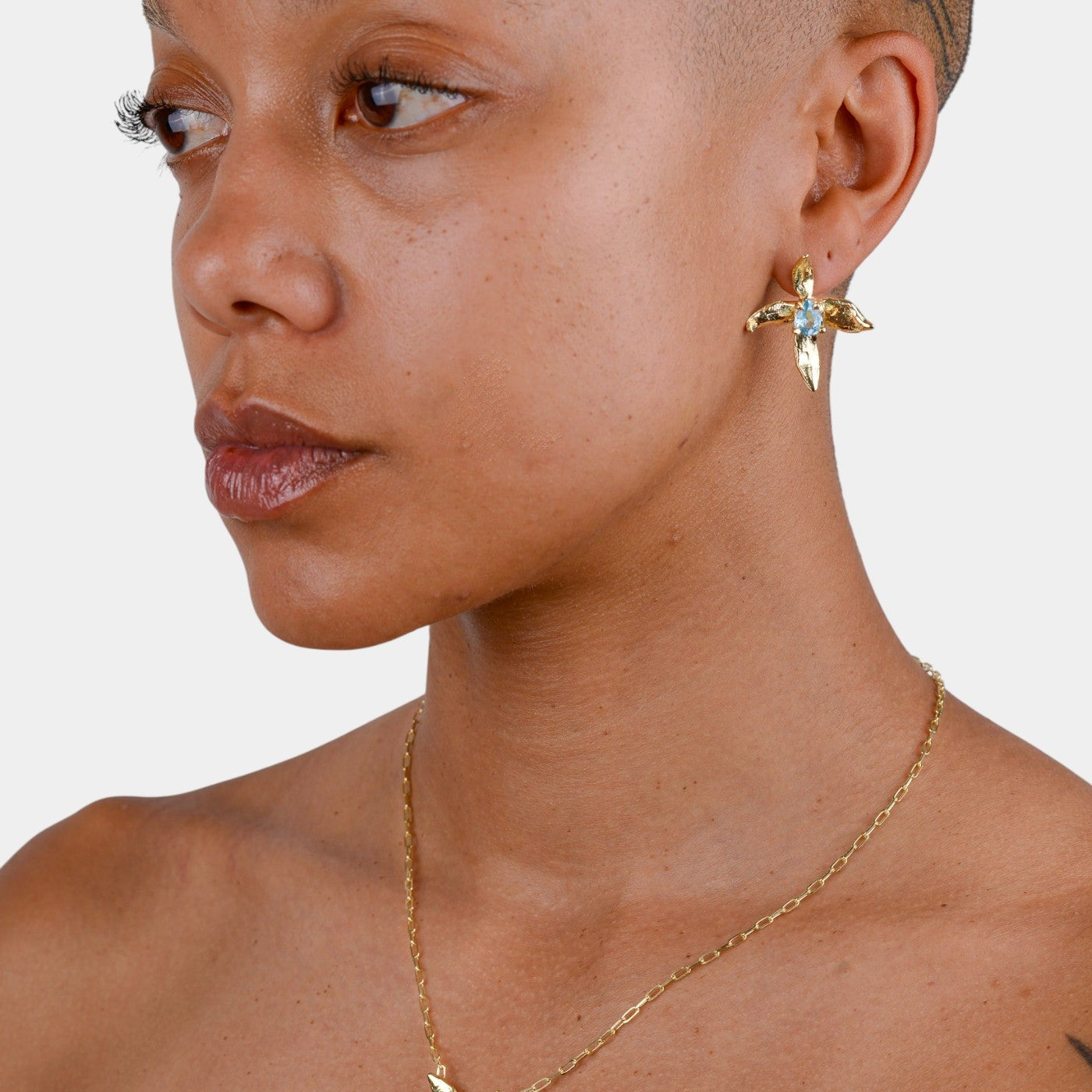 Close-up of a person wearing gold earrings and necklace with gemstones on a plain background