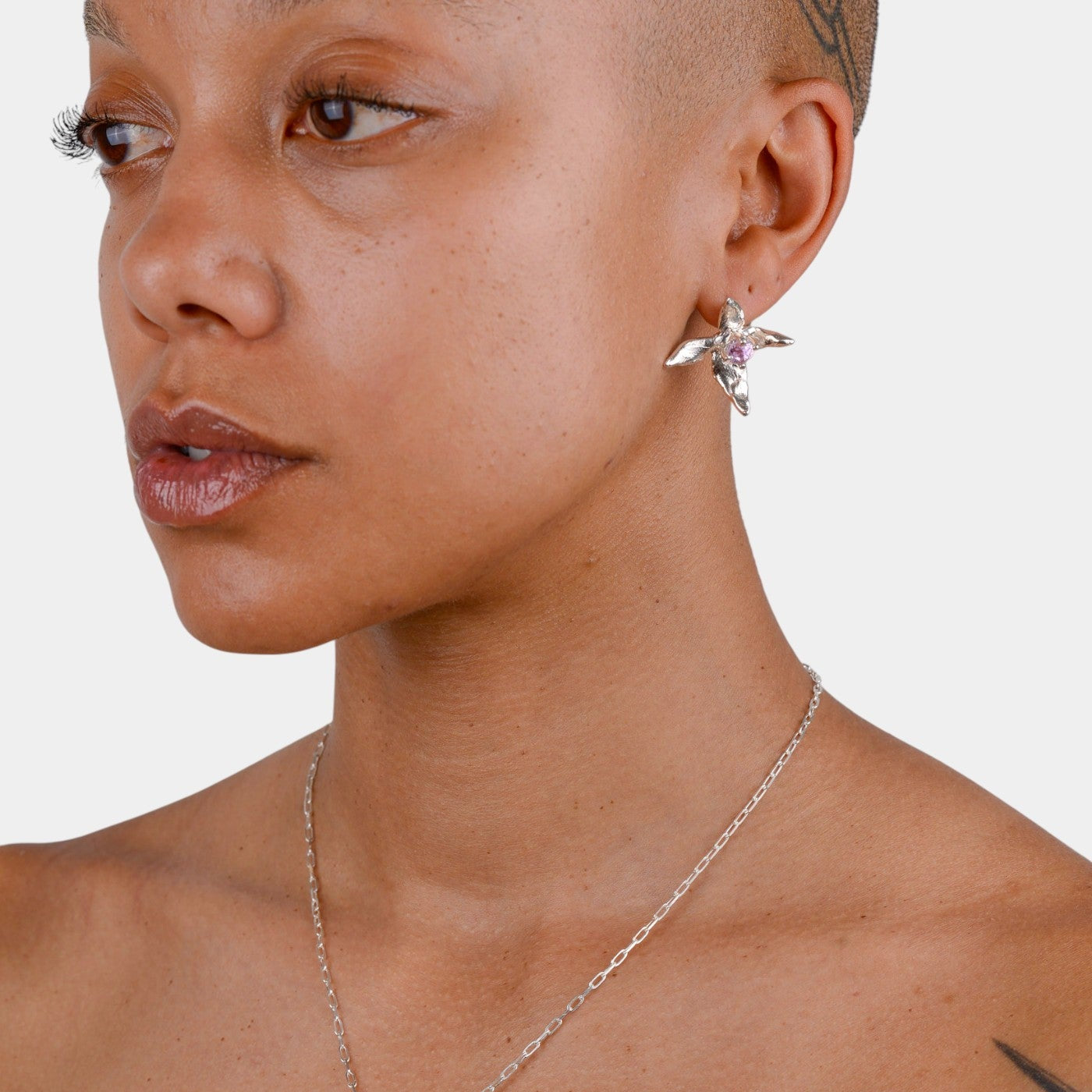 Close-up of a person wearing x-shaped earrings and necklace on a white background