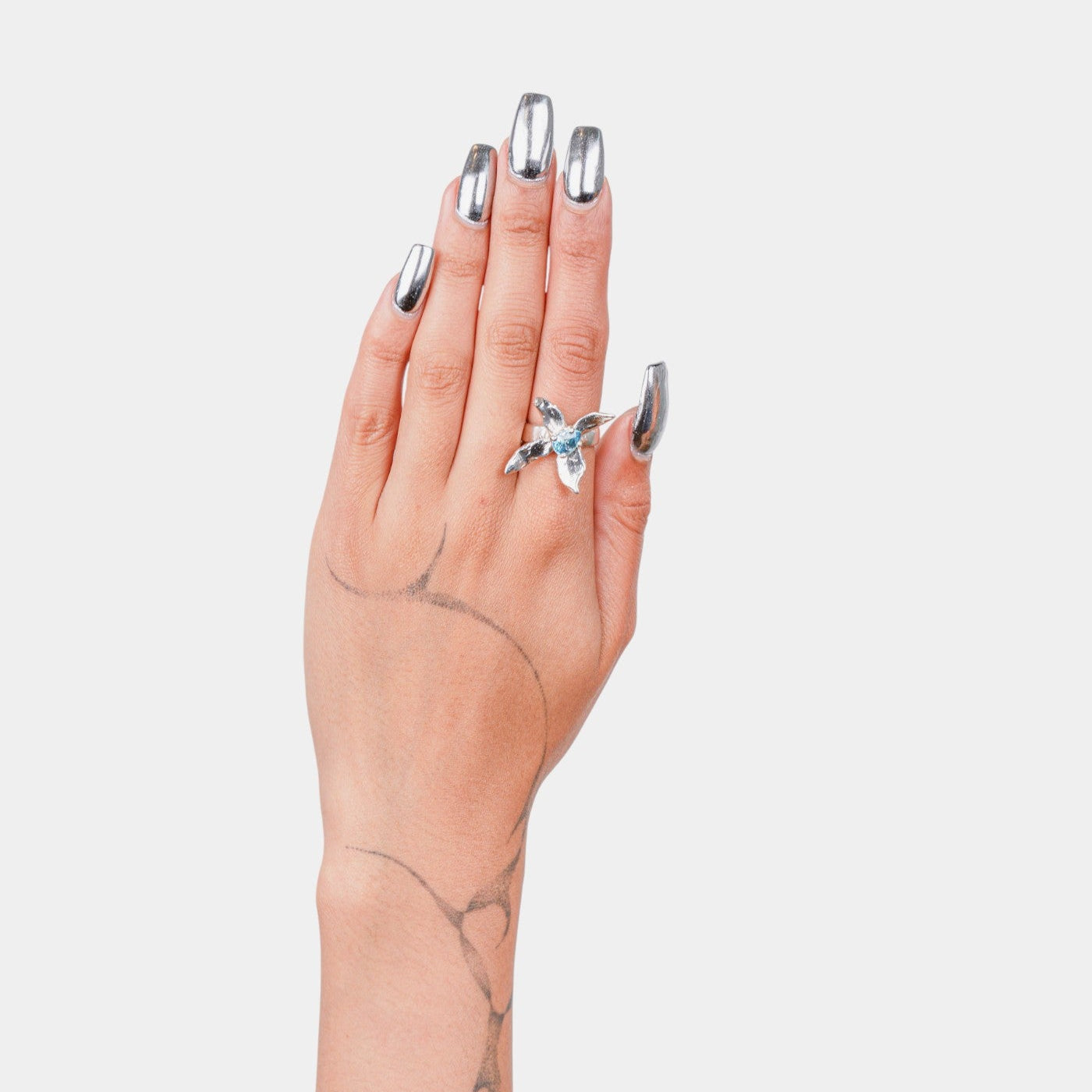 Hand with silver nail polish and a silver ring on a light gray background