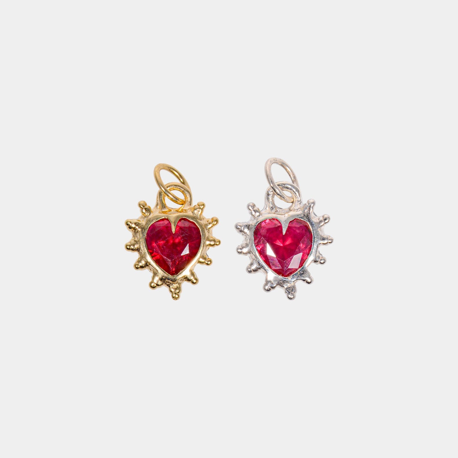 Two heart-shaped pendants, one with a ruby red CZ in a gold setting, and the other in a silver setting.