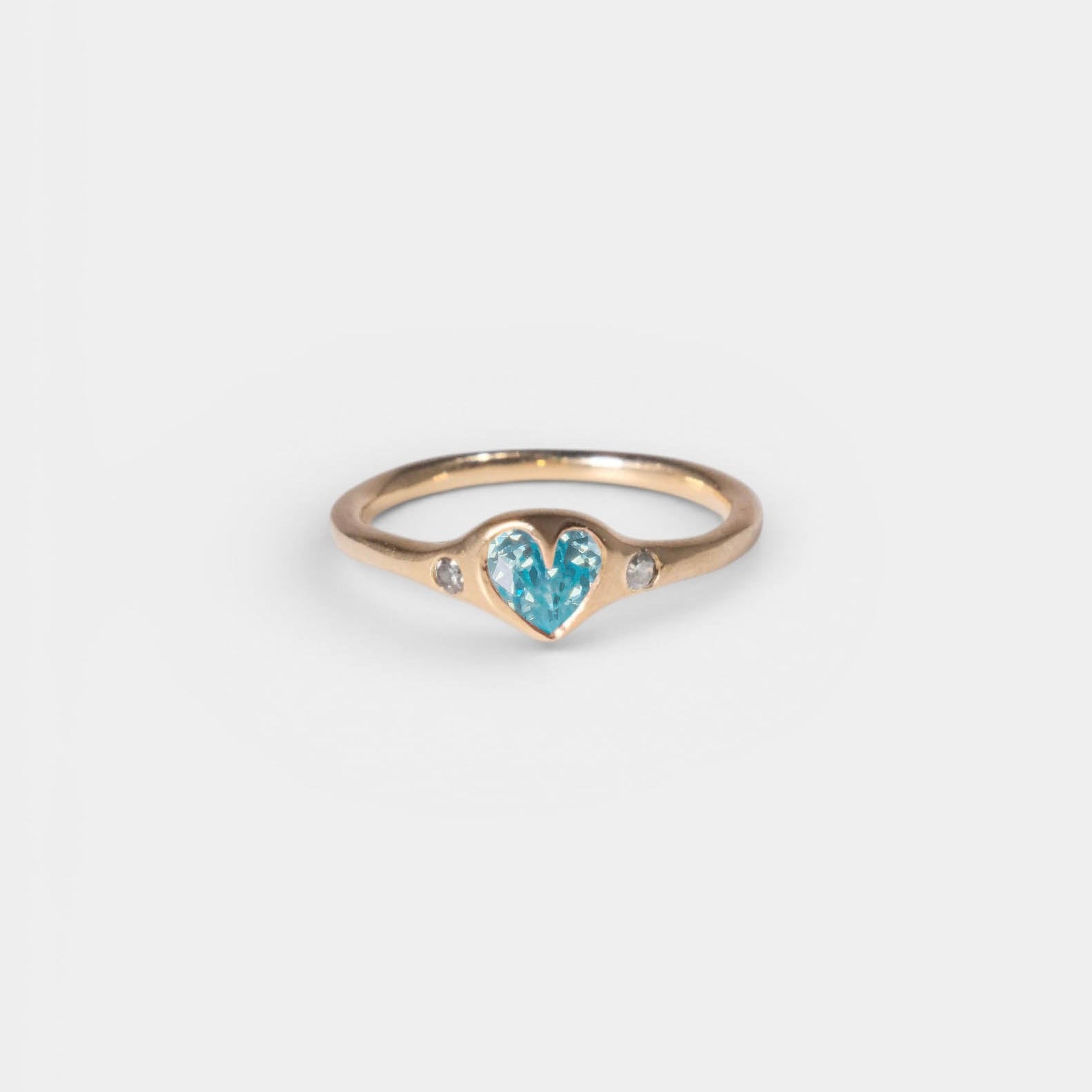 Gold ring with a heart-shaped blue gemstone on a light gray background