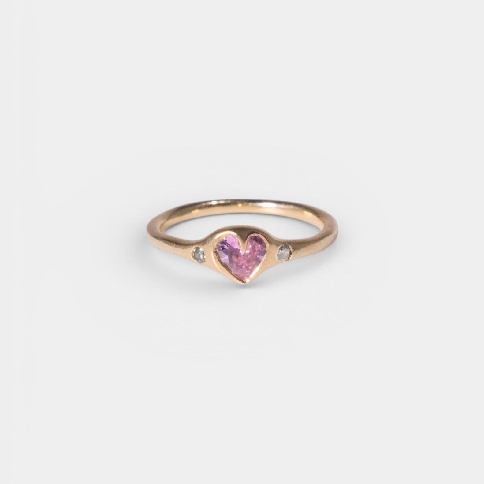Gold ring with a pink heart-shaped gem on a light gray background